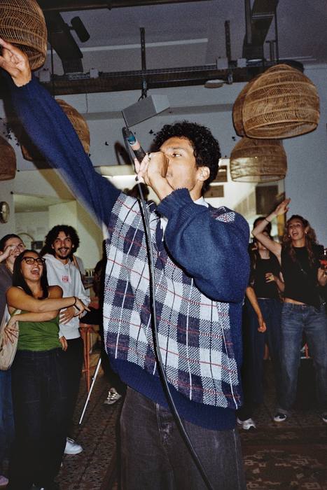 Chanteur au micro, bras levé vers les suspensions en osier, photo argentique